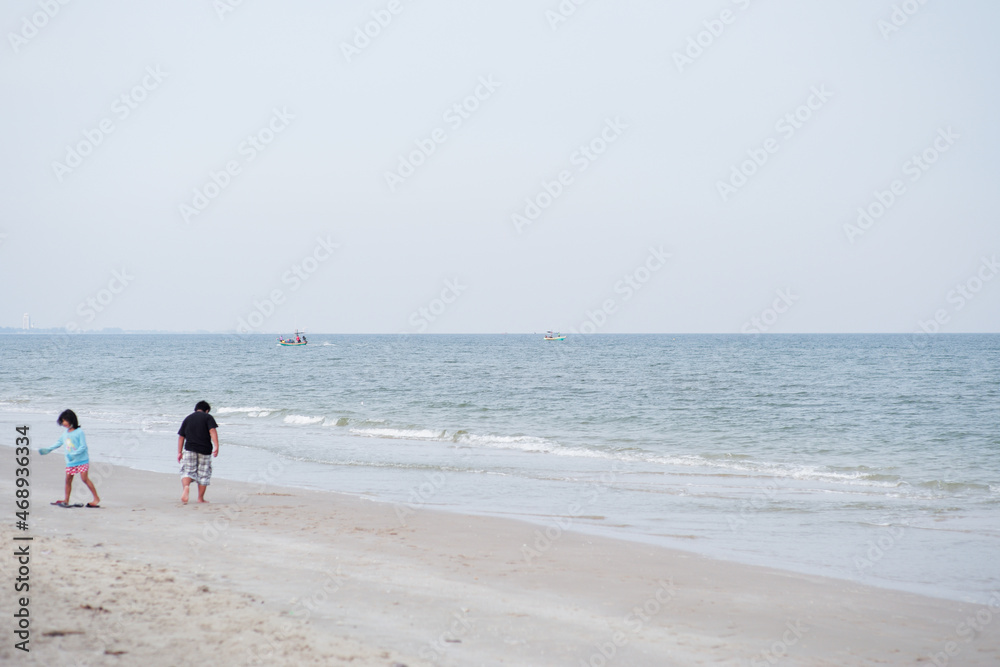 Seascape with fishing boat floating in the sea with blurred foreground of little boy and girl playing on the beach