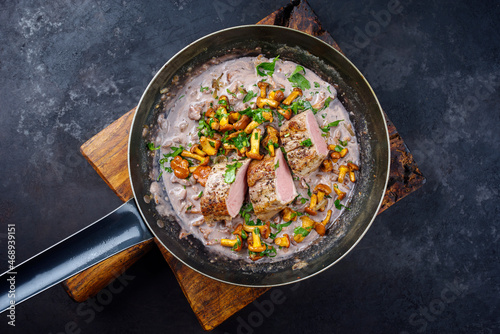 Fried dry aged pork fillet chateaubriand medallion steak natural with chanterelles in walnut cream sauce served as top view in a classic skillet on black background