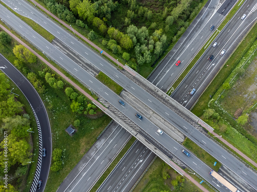 Drone aerial top down shot of cars and traffic driving on the motorway surrounded by green grass and trees. View from above