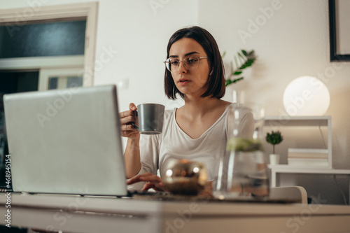 Woman drinking coffee and using a laptop while working from home
