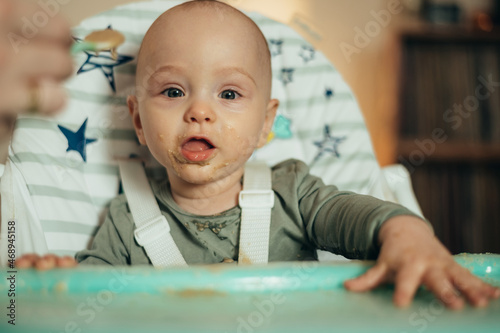 Baby eating with a face stained in food while in a child's dining chair