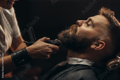 Leinwand Poster Young bearded man getting beard haircut by hairdresser