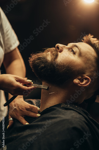 Man getting shaved with straight edge razor by hairdresser at barbershop photo