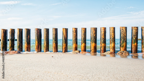 Wooden breakwater on the sandy shore, washed by the waves against the background of the sea