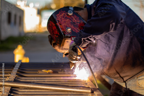 Fotografia Welder welding a grating wearing a welder helmet with a beautiful welding flash