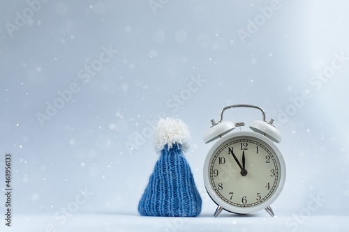 Set of Christmas accessories, a clock and a blue knitted cap on a light snow background. Concept New Year, Christmas.