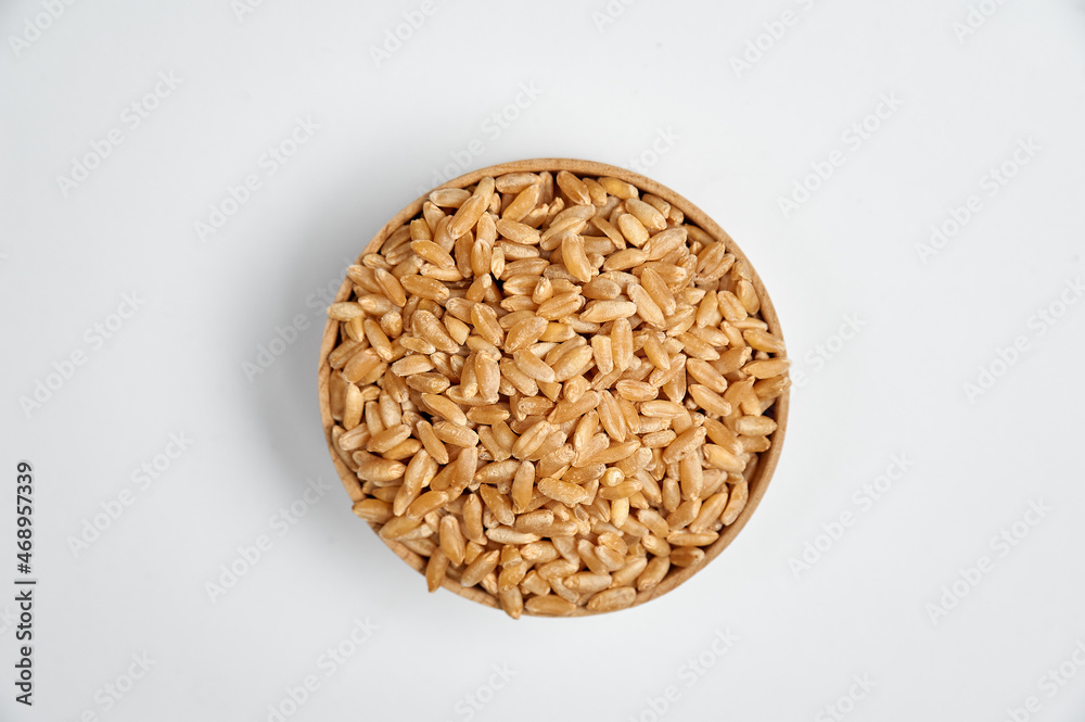 peeled wheat grain in a wooden bowl on a white background