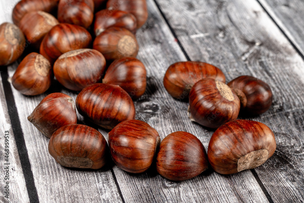 some raw chestnuts, marron (Castanea sativa), a classic autumn fruit, on light colored wooden rustic background with selective focus on foreground. some raw chestnuts, marron (Castanea sativa), a classic autumn fruit, on light colored wooden rustic background with selective focus on foreground.