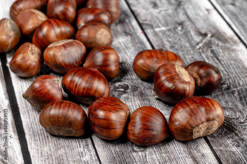 some raw chestnuts, marron (Castanea sativa), a classic autumn fruit, on light colored wooden rustic background with selective focus on foreground.
