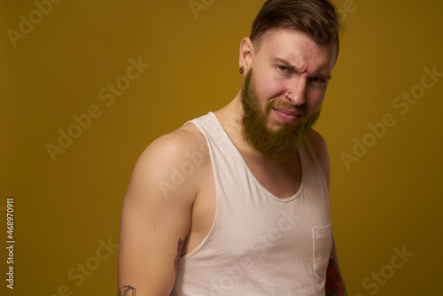 a bearded man with a serious expression in a white t-shirt with tattoos on his arms