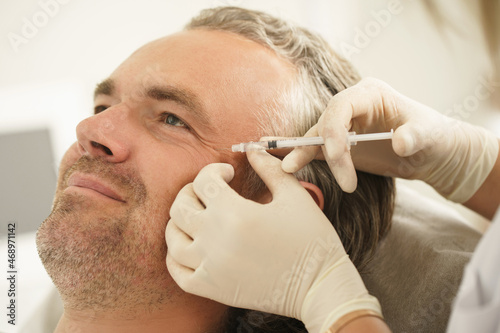 Middle aged male client during filler injections in a clinic photo