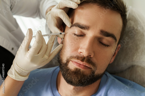 Female doctor and male client during filler injections in clinic photo