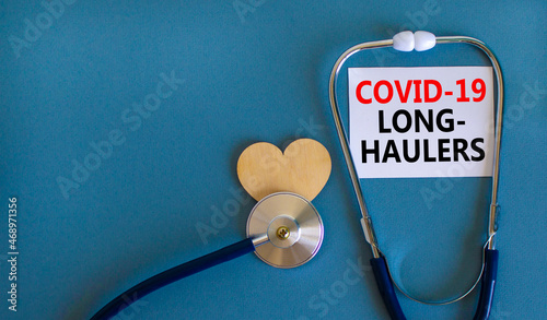 COVID-19 long-haulers covid symptoms symbol. White card with words Covid-19 long-haulers. Wooden heart, stethoscope, blue background, copy space. Medical, COVID-19 long-haulers covid symptoms concept.