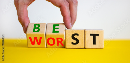 Best or worst symbol. Businessman turns wooden cubes and changes the word best to worst. Beautiful yellow table, white background, copy space. Business and best or worst concept.