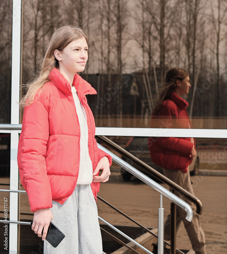 teenager girl wearing bright jacket going downstaris in a city and holding a smartphone photo