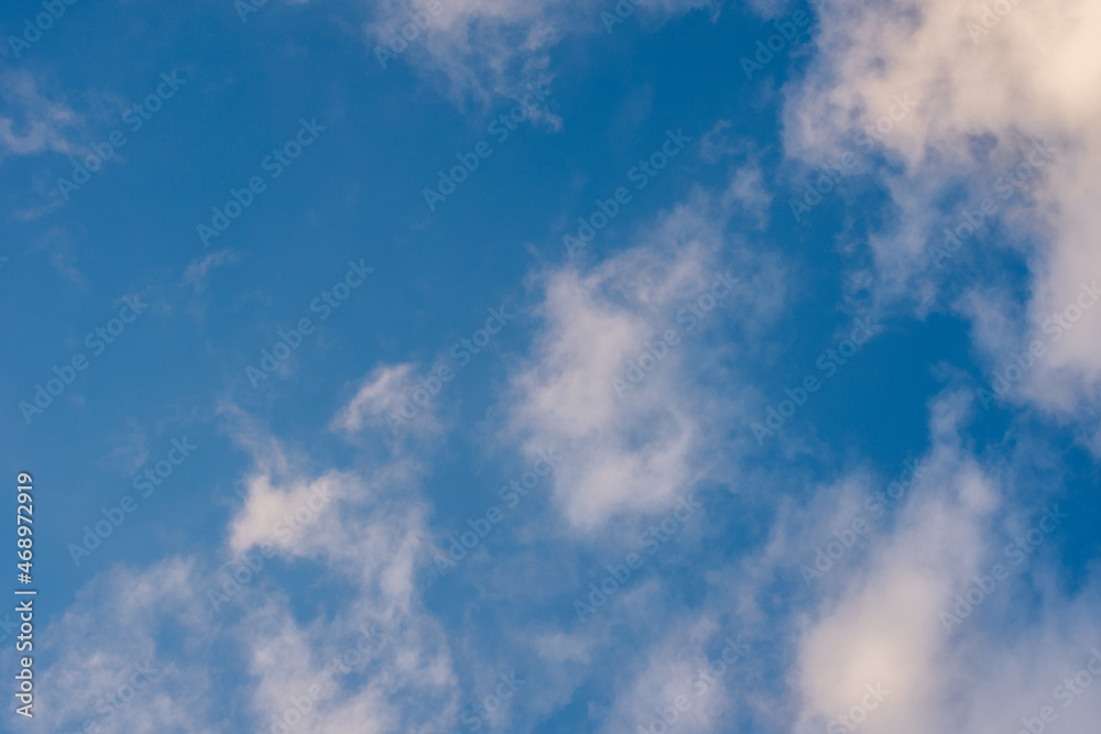 Obraz premium Blue sky with white fluffy glowing clouds. The clouds are lit by the dawn or setting sun. A beautiful natural sky background