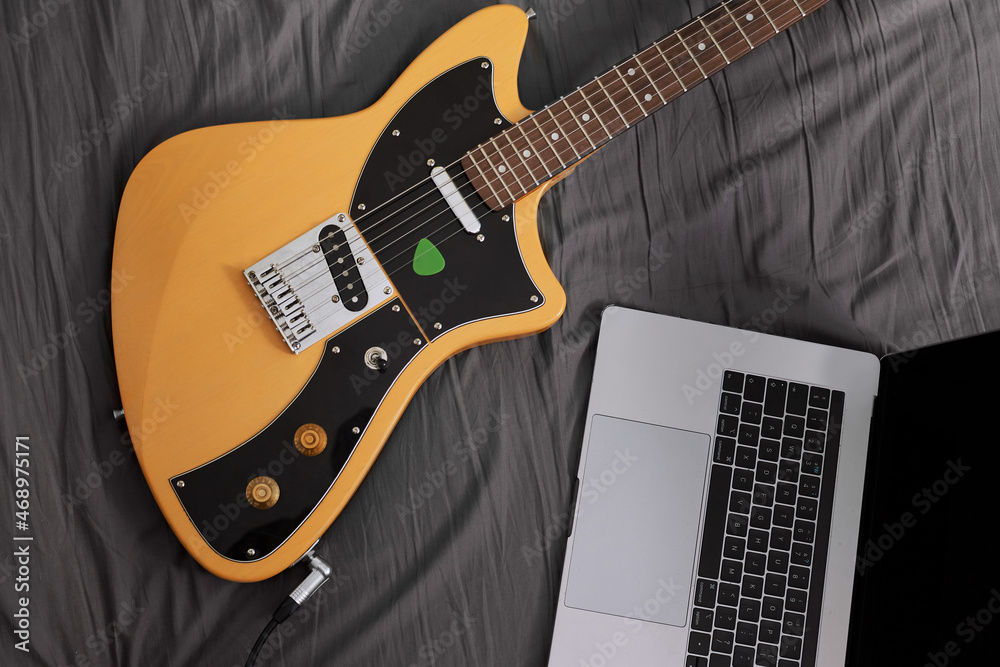 Naklejka premium Electric guitar and laptop laying on a bed