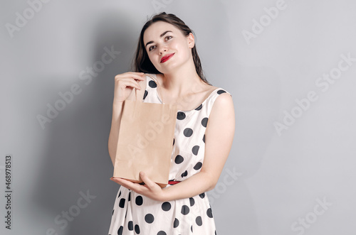 Portrait of a beautiful woman. Dressed in a polka dot dress. Stands with a paper craft bag. Successful shopping. Surprise.