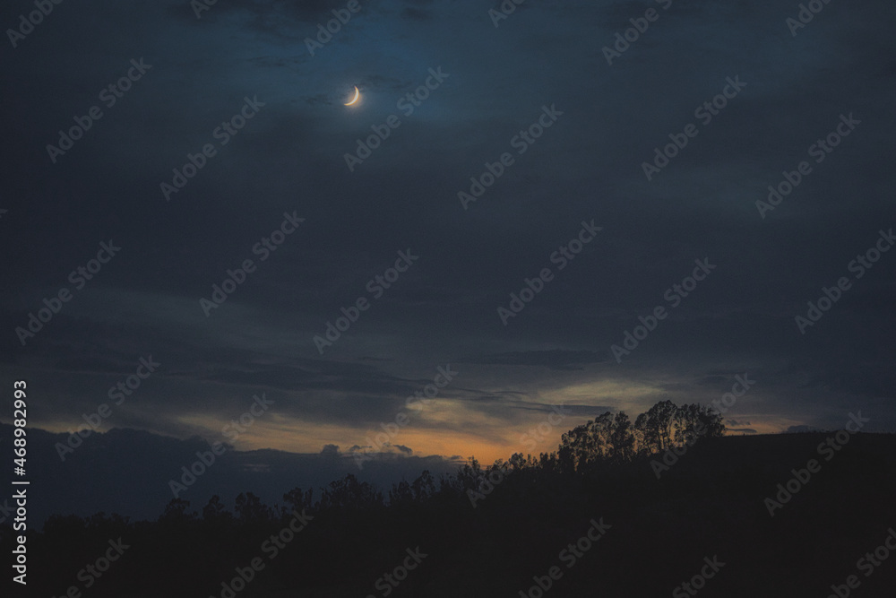 Obraz premium Cloudy sky at sunset with crescent moon.