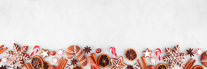 Christmas baking bottom border with cookies, peppermints and spices. Top view over a white marble background with copy space. Holiday baking concept.