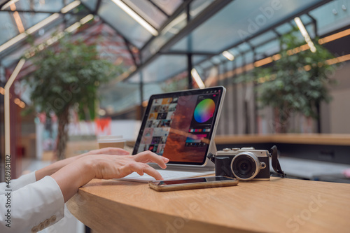 A photographer or retoucher works remotely with a laptop in a public space or coworking. A young woman in a white jacket works with images, a designer or a social media manager photo