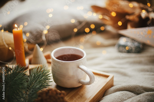 Warm cup of tea on bed with christmas stars  golden lights  pine trees  candle. Magic winter Hygge
