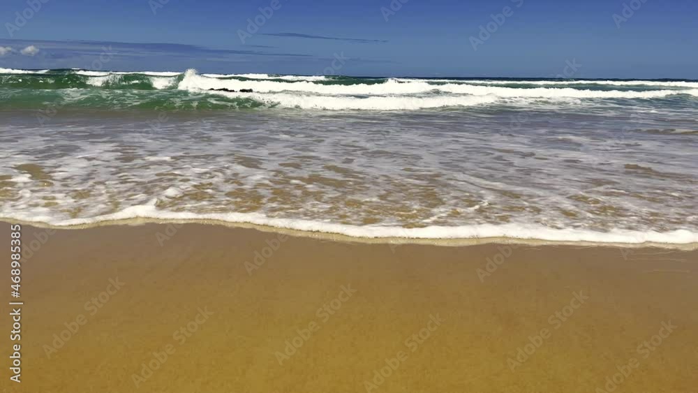Slow motion scene of waves on sandy beach with blue sky cackground. Suitible as wallpaper, relaxing background, advertising design etc.,