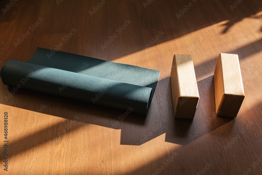 Closeup of two wooden yoga blocks and blue yoga mat on the wooden floor. - obrazy, fototapety, plakaty 