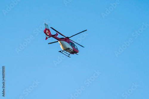 Red white helicopter flying in clear blue sky