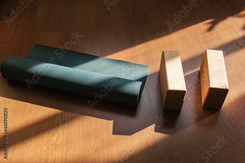 Closeup of two wooden yoga blocks and blue yoga mat on the wooden floor.