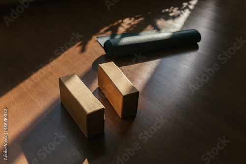 Closeup of two wooden yoga blocks and blue yoga mat on the wooden floor.