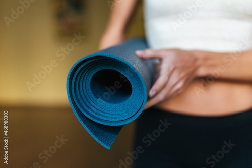 Close-up of a girl holding a blue yoga mat in her hands.