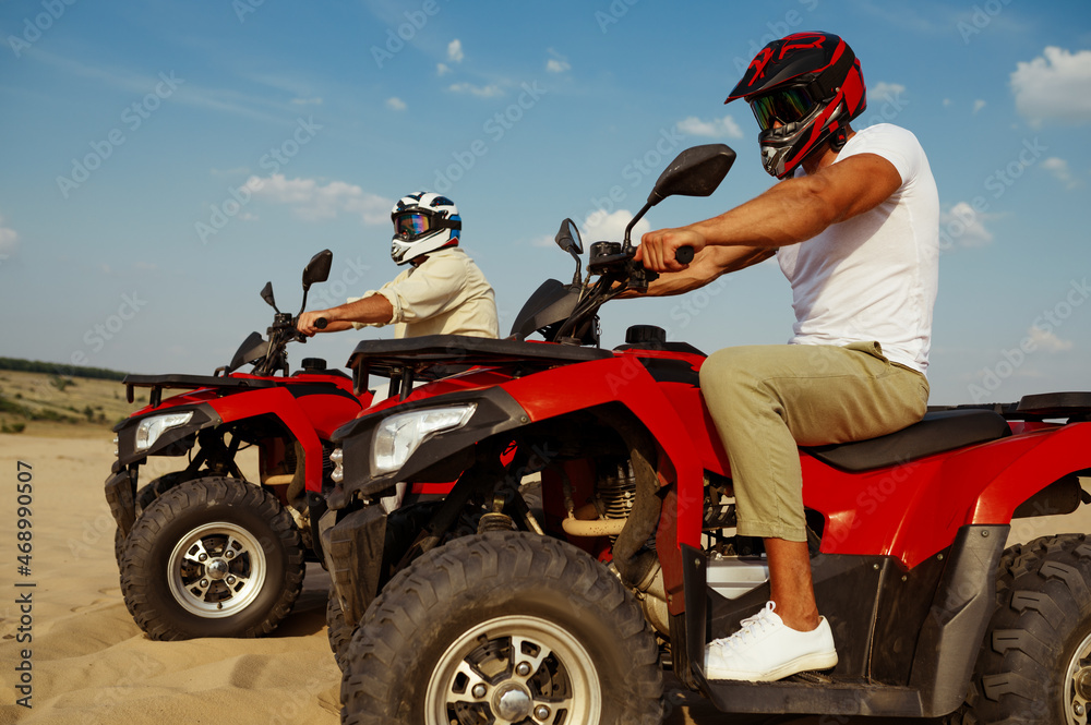 Men in helmets and glasses ride on atv in desert