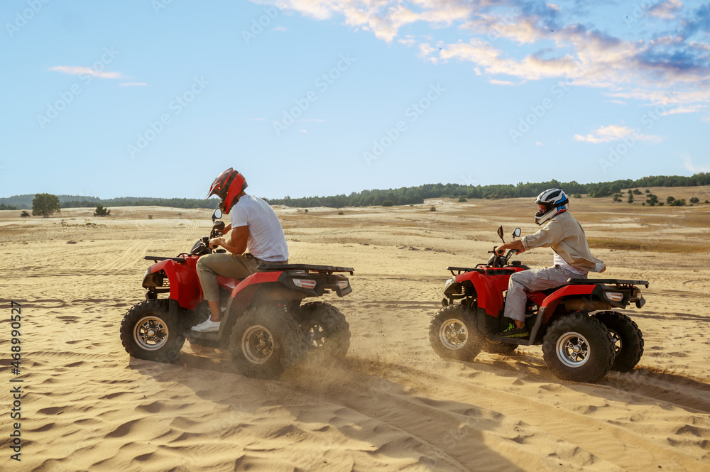 Two men in helmets ride on atv in desert Two men in helmets ride on atv in desert