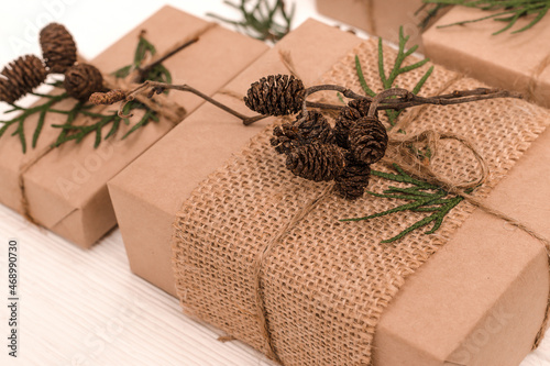 Festive decoration of gifts in eco-style.Gift boxes are wrapped in craft paper,tied with cotton thread,decorated with thuja leaves,cones and burlap.Christmas,New Year and eco-friendly concept.