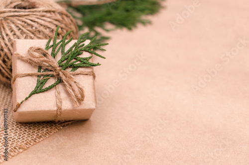 Festive decoration of gift in eco-style.Gift box is wrapped in craft paper,tied with cotton thread,decorated with thuja leaves and burlap.Christmas,New Year and eco-friendly concept.Copy space.