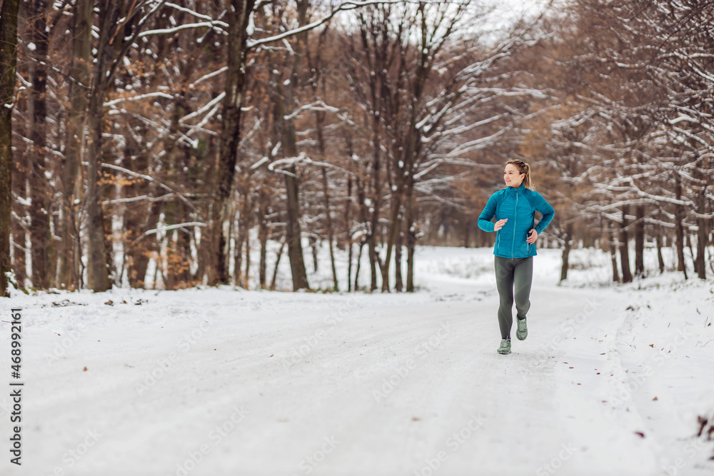 Slim sportswoman jogging in nature on a snowy weather. Cold weather, snow, healthy life, fitness, healthy habits