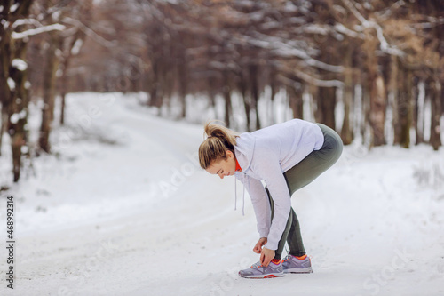 Sportswoman standing on snow in nature at winter and tying shoelace. Sneakers, winter fitness, healthy life, nature