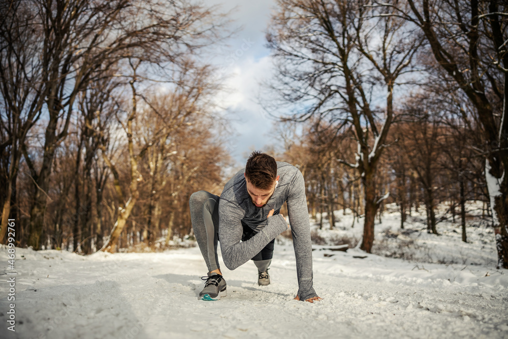 Fototapeta premium Fit sportsman doing warm up and stretching exercises while kneeling in nature at snowy winter day. Winter fitness, healthy lifestyle