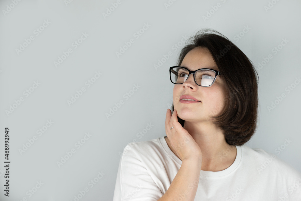 Studio photo on a gray background of a beautiful smiling dreaming girl with dark hair wearing glasses