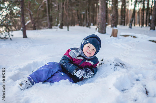 Happy boy enjoys winter season and lies in the snow in forest on sunny winter day. Lovely winter scenery, active weekend, seasonal outdoor activities, happy family lifestyle