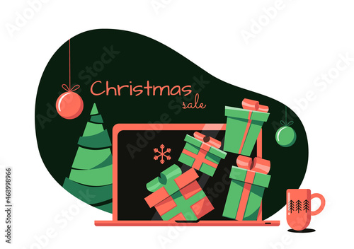 Online christmas sale concept. Dark background, gifts of green and red colors peep out of a laptop standing on the table, next to it there is a mug with a Christmas ornament and a small Christmas tree