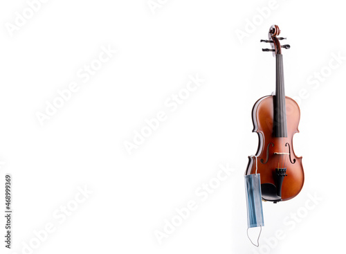 A brown violin or viola from wood on a white background with a medical mask hanging off of one of its pegs No.6