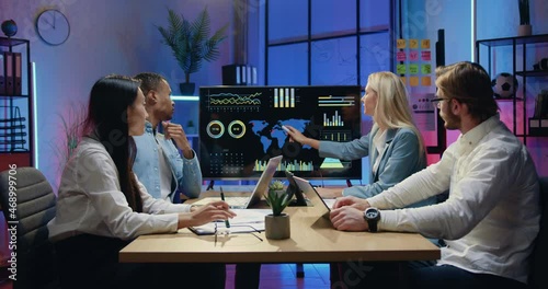 Business concept where attractive confident responsible skilled diverse teammates browsing world statistic indicators on tv screen during joint meeting in evening office photo