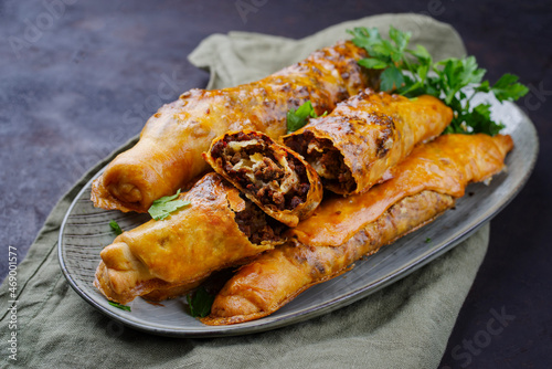 Traditional Turkish crispy sigara borek rolls with minced meat rolled in fillo pastry served as close-up in a Nordic design plate on a black board photo