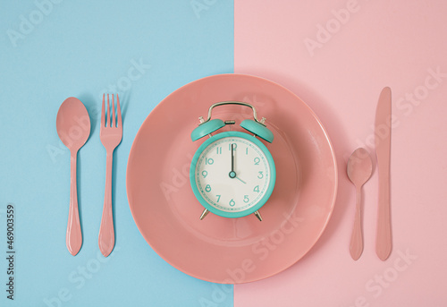 Minimalist concept idea light blue alarm clock on pink plate with vintage color background on pop art style with fitnes and diet idea. Eat on time and smart