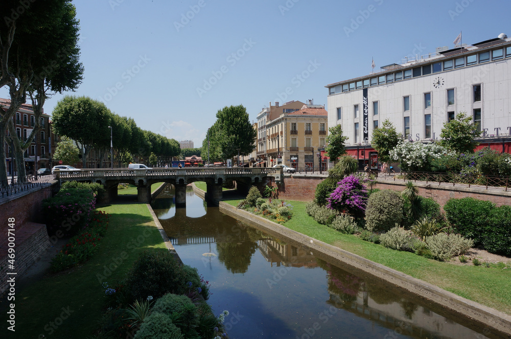 a bridge over a river in France on a sunny summer day surrounded by flowers and trees