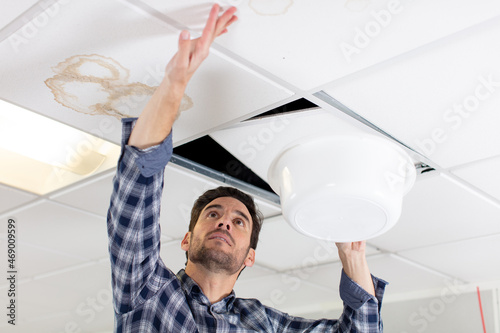 man holds bowl under leak in ceiling panel