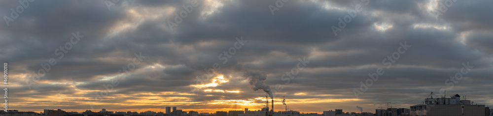 Wide panorama of cloudy sunrise or sunset over rooftops