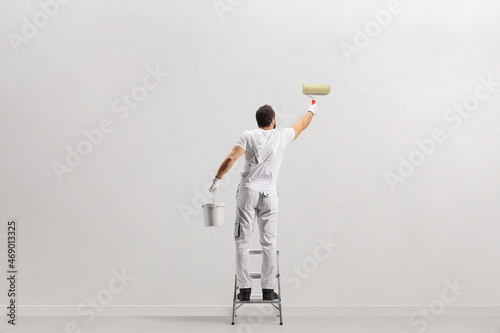 Fototapeta Naklejka Na Ścianę i Meble -  Rear view shot of a painter holding a bucket and painting a wall on a leader